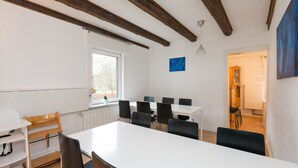 Ein Konferenzraum mit weißem Tisch, schwarzen Stühlen, Holzbalken, einem Fenster und einem blauen Gemälde.