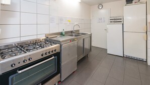 Eine Küche mit Gasherd, Backofen, Spüle aus Edelstahl und einem weißen Kühlschrank.