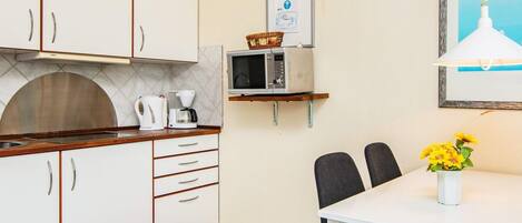 A compact kitchen with white cabinets, a microwave, a coffee maker, and a small dining table with chairs.