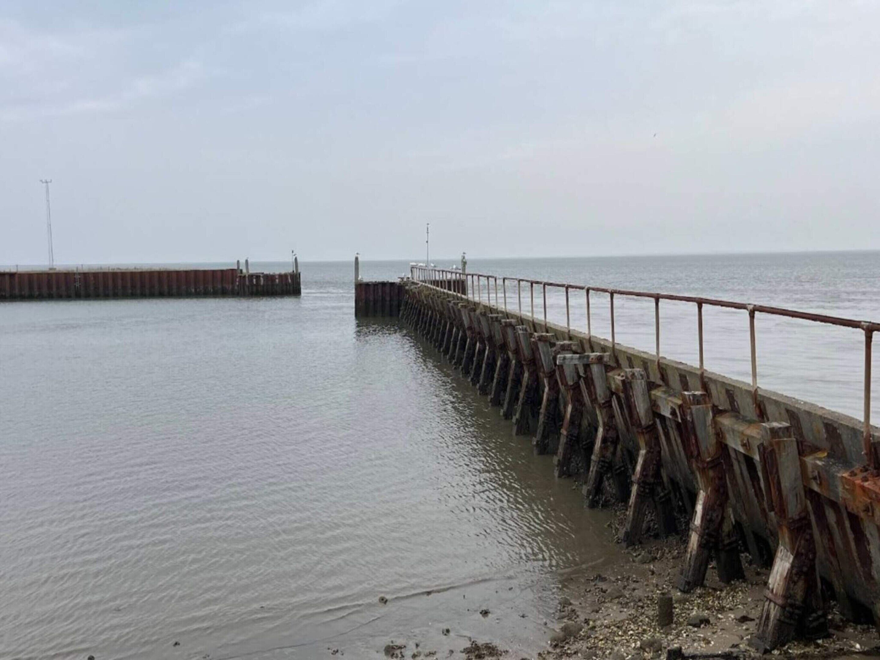 A pier extending into calm waters with a metal railing and wooden posts.