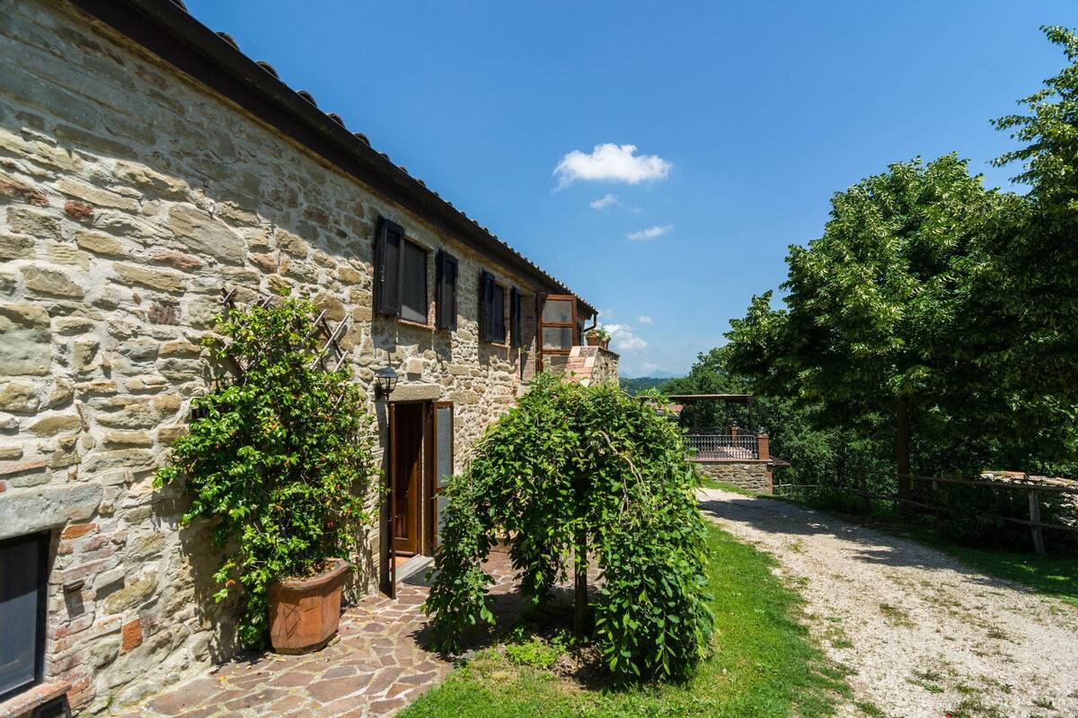 A stone building with a rustic exterior, a paved courtyard, and a well-maintained garden with two large potted plants.