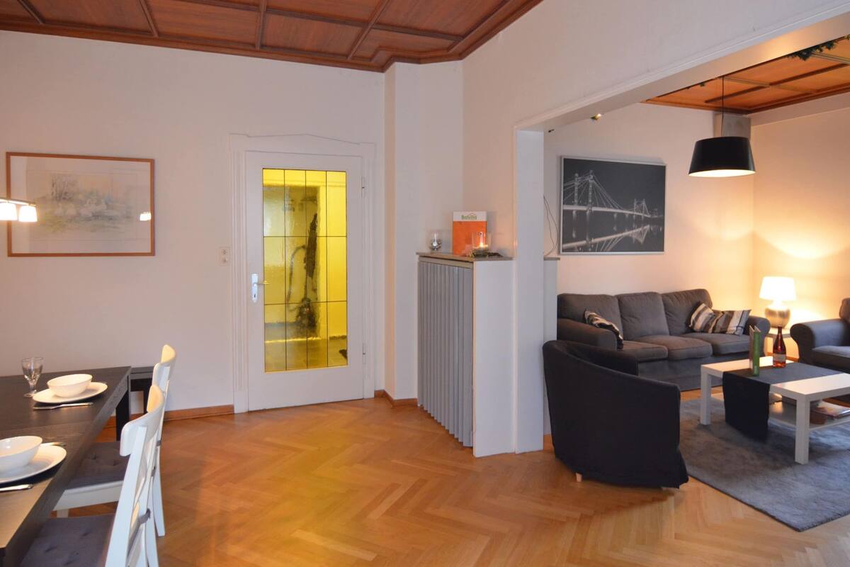 Een moderne woonkamer met een bank, een eettafel met stoelen, een radiator en een schilderij aan de muur.