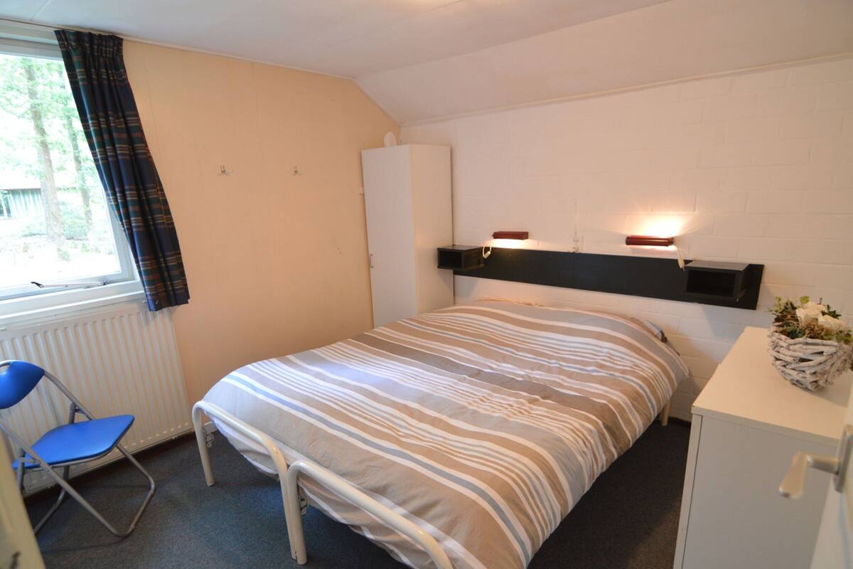 A small, neatly arranged bedroom with a bed, a chair, a desk, and a radiator.