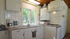 A compact kitchen with white cabinets, a built-in stove, and a window providing natural light. - Completely Detached Bungalow in a Nature-filled Park by a Large fen (Stramproy)