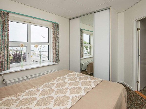 A bedroom with a bed, a window with curtains, a radiator, and a mirror.