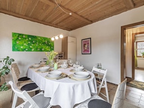 Zona pranzo con tavolo rotondo apparecchiato per sei persone, circondato da sedie bianche.