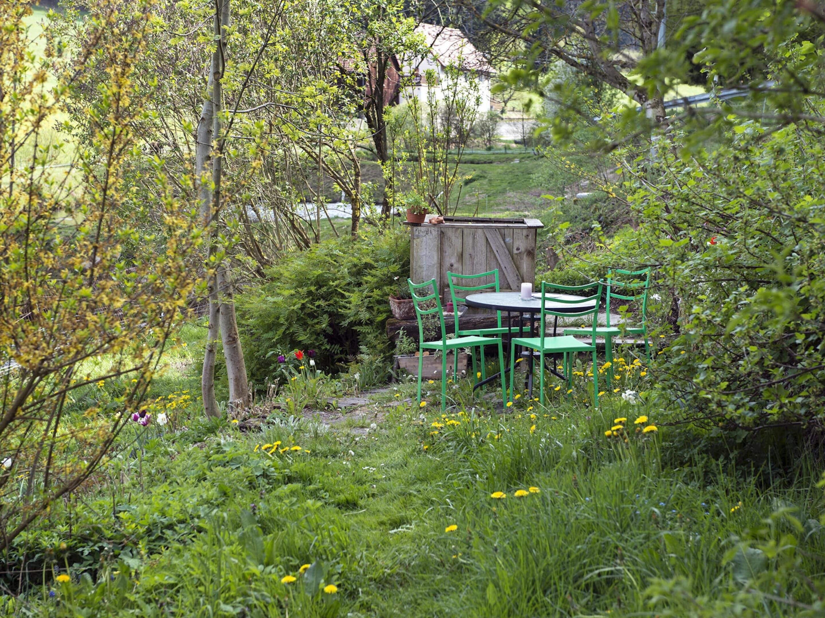 A garden with a wooden shed, green chairs, and a table.