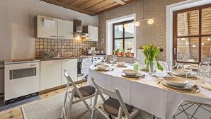 Een moderne keuken met een eethoek, gedekt voor een maaltijd, met houten balken, een groot raam en uitzicht op de omgeving.