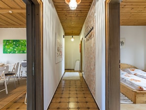 Un corridoio con soffitto in legno, pavimento a motivi esagonali e un letto con copriletto floreale sulla destra.