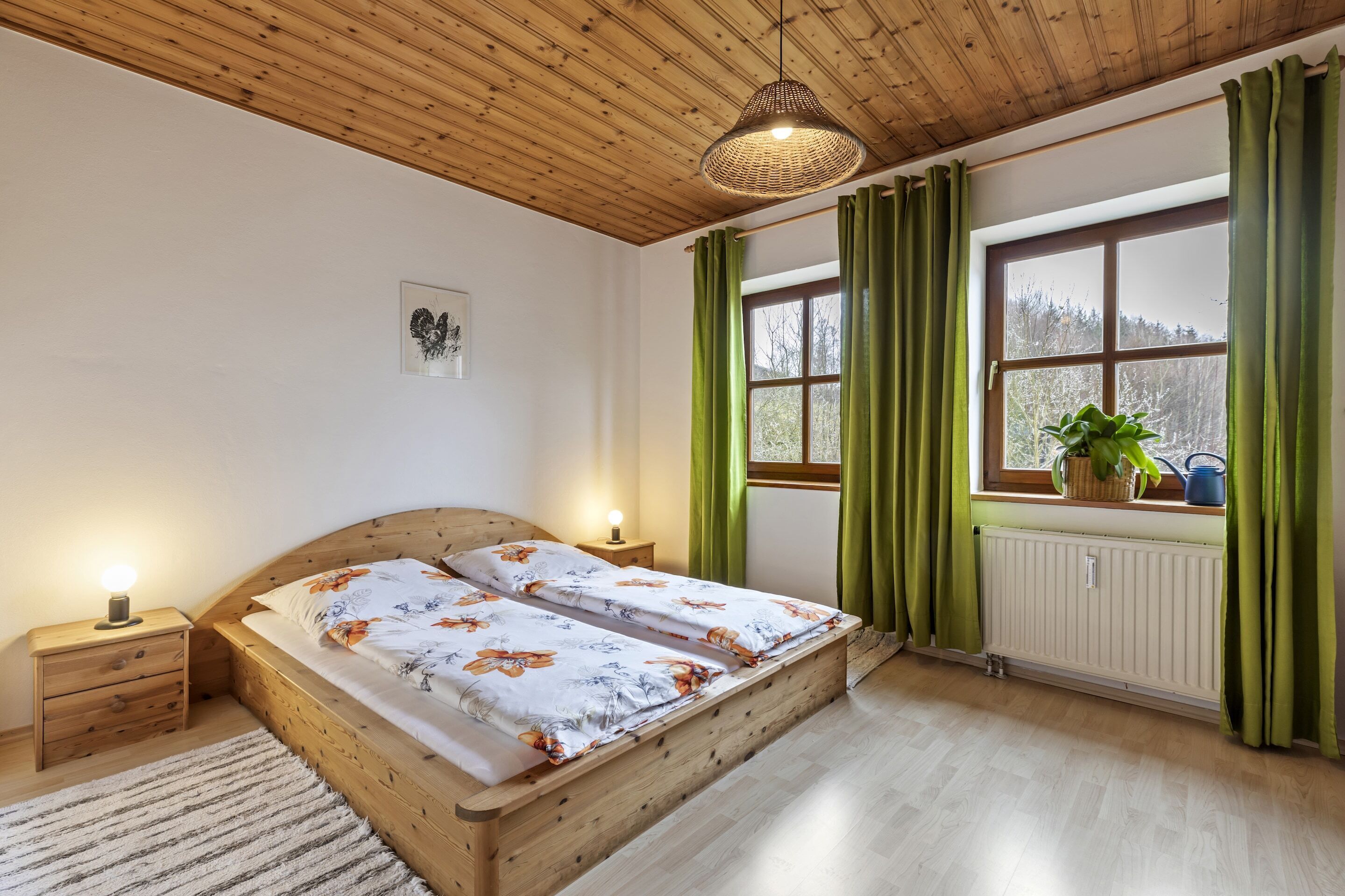 A wooden-framed bed with floral bedding, a bedside lamp, and a window with green curtains.