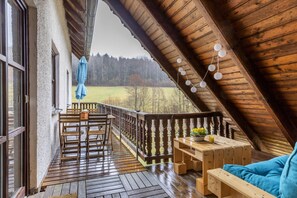 Una stanza mansardata con travi in legno, un tavolo di legno con una pianta e vista su un campo verde.