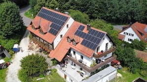 Een huis met twee verdiepingen en zonnepanelen op het dak, omringd door groen.