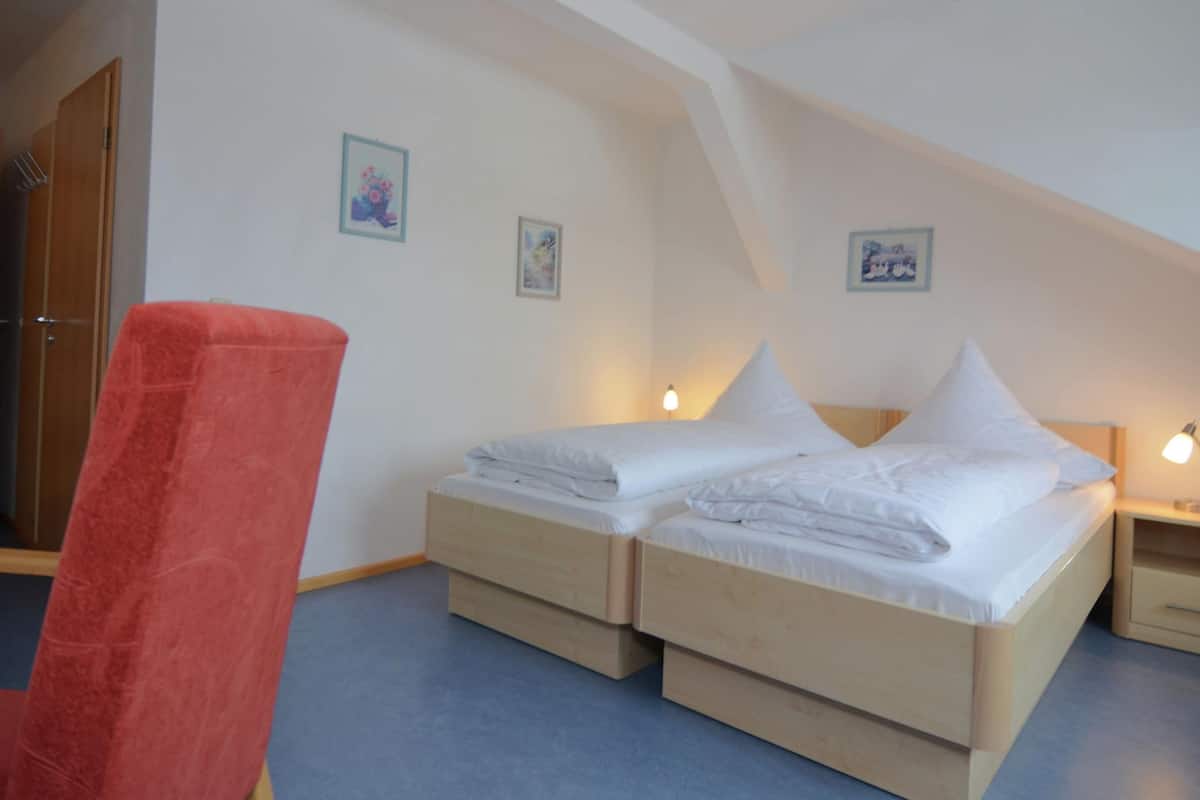 A room with two beds, a red chair, and a wooden wardrobe.