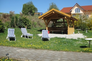 A gazebo with a table and chairs, surrounded by a grassy area with yellow flowers. - Comfortable Apartments in Rotthalmunster (Rotthalmuenster)
