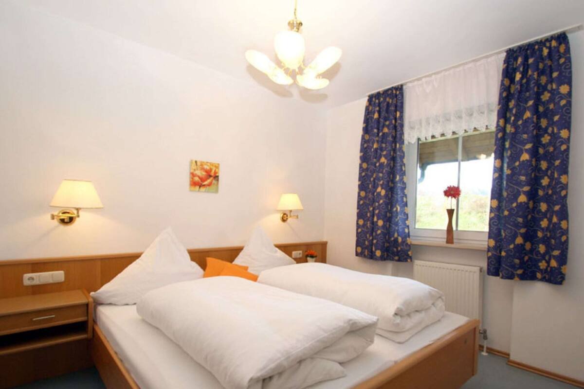 Une chambre d’hôtel avec un lit double, deux tables de chevet, une commode, une fenêtre avec des rideaux et un luminaire au plafond.