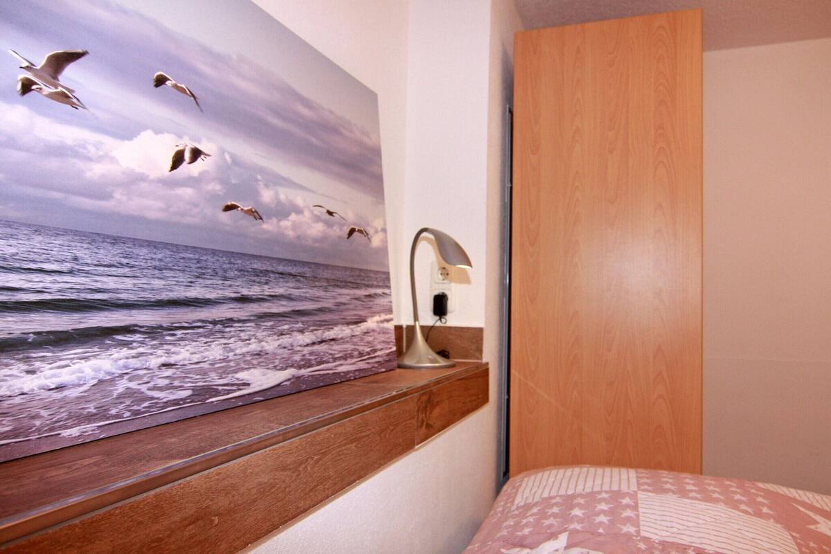 A bedroom with a large window overlooking the sea, a wooden headboard, and a bed with a patterned bedspread.