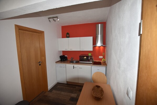 Cocina compacta con armarios blancos, un microondas y una campana extractora de acero inoxidable.