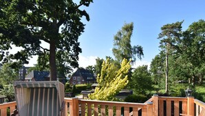 Eine Holzterrasse mit gepolstertem Sitz einer Bank und einem Stuhl, umgeben von einem Hollerleger.