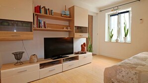 Ein modernes Schlafzimmer mit Flachbildfernseher, Holzböden, einem Bett mit floralem Überwurf und einem Fenster mit Pflanzen.