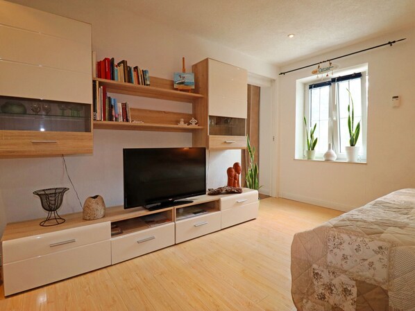 Un dormitorio moderno con una televisión de pantalla plana, estanterías de madera, una cama con colcha estampada y un ventanal con plantas.