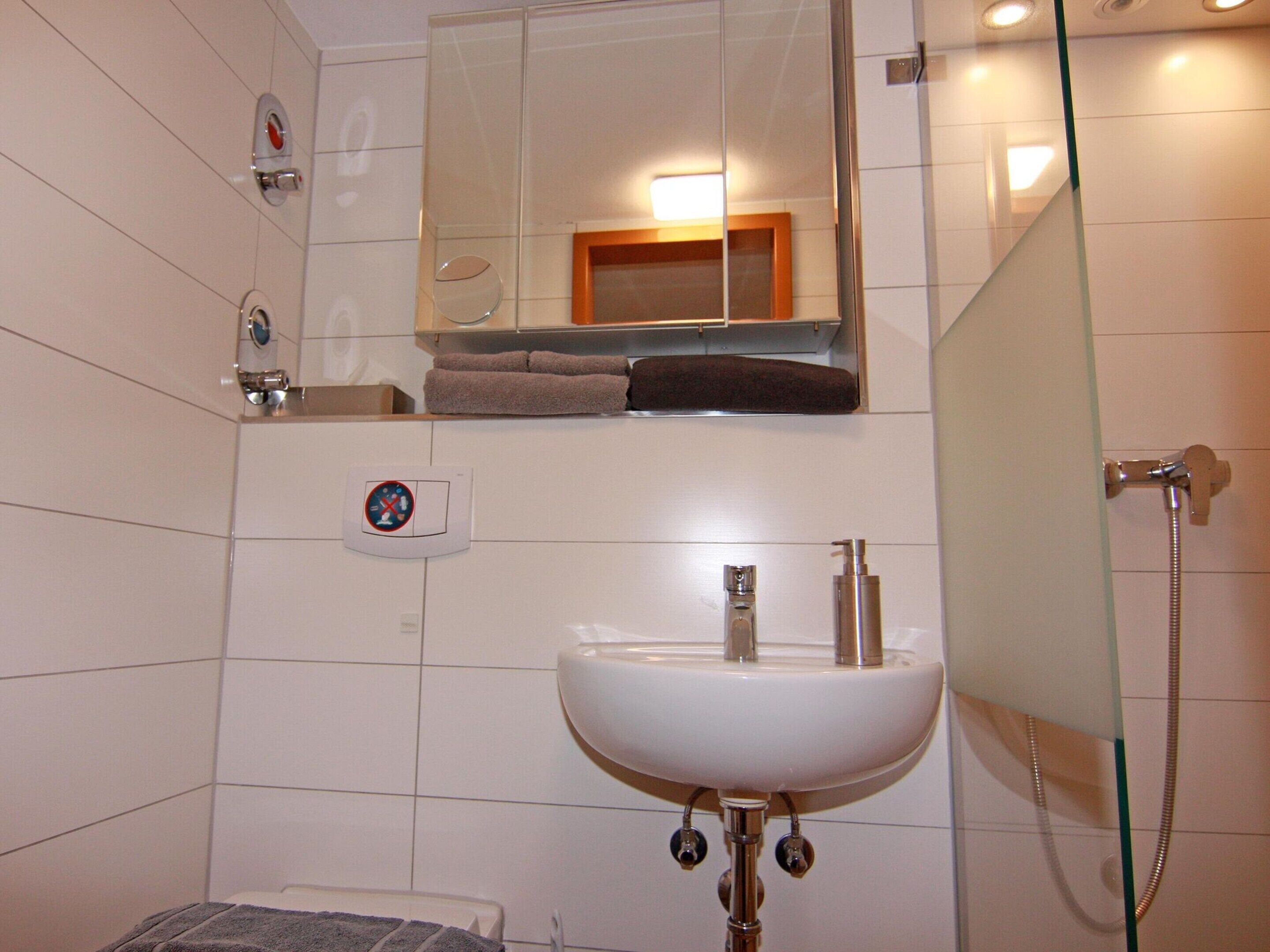 Un baño con lavamanos blanco, cabina de ducha de vidrio y espejo sobre el lavamanos.