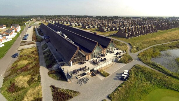 A modern building with a unique roof design, surrounded by a residential area with uniform houses. - 4 Person Holiday Home on a Holiday Park in Romo (Rømø)