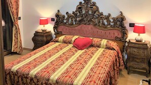 Ein Schlafzimmer mit einem großen, verzierten Bett, zwei Nachttischlampen und einem Vorhang auf der linken Seite.
