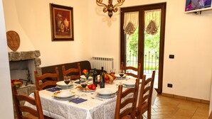 Ein Esszimmer mit einem für sechs Personen gedeckten Tisch, Holzsesseln, einer Kristallleuchtre, einem Kamin und einem Fenster mit Blick auf Grünflächen.