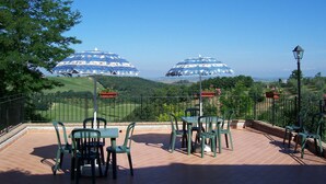 A terrace with a table and chairs, overlooking a scenic landscape with two domed structures. - Lavish Holiday Home in Volterra With Pool (Volterra)