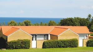 Una fila di edifici in mattoni con tetti in tegole arancioni e cornici bianche, con vista sul mare.