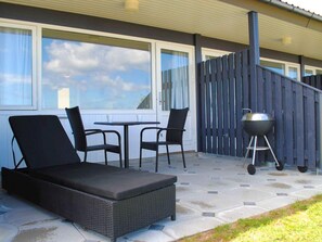 Une terrasse extérieure avec un canapé en osier, deux fauteuils, une petite table et un barbecue.