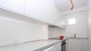 A modern kitchen with white cabinets, a granite countertop, a built-in oven, and a window above the sink. - 4 Person Holiday Home in Allinge (Allinge)