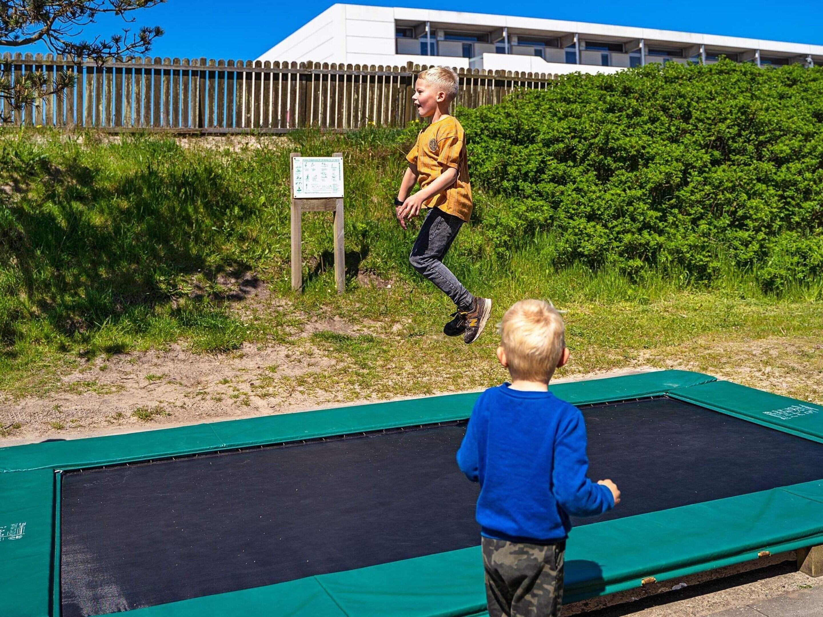 Un enfant qui saute sur un trampoline, avec une clôture en bois et de la verdure en arrière-plan.