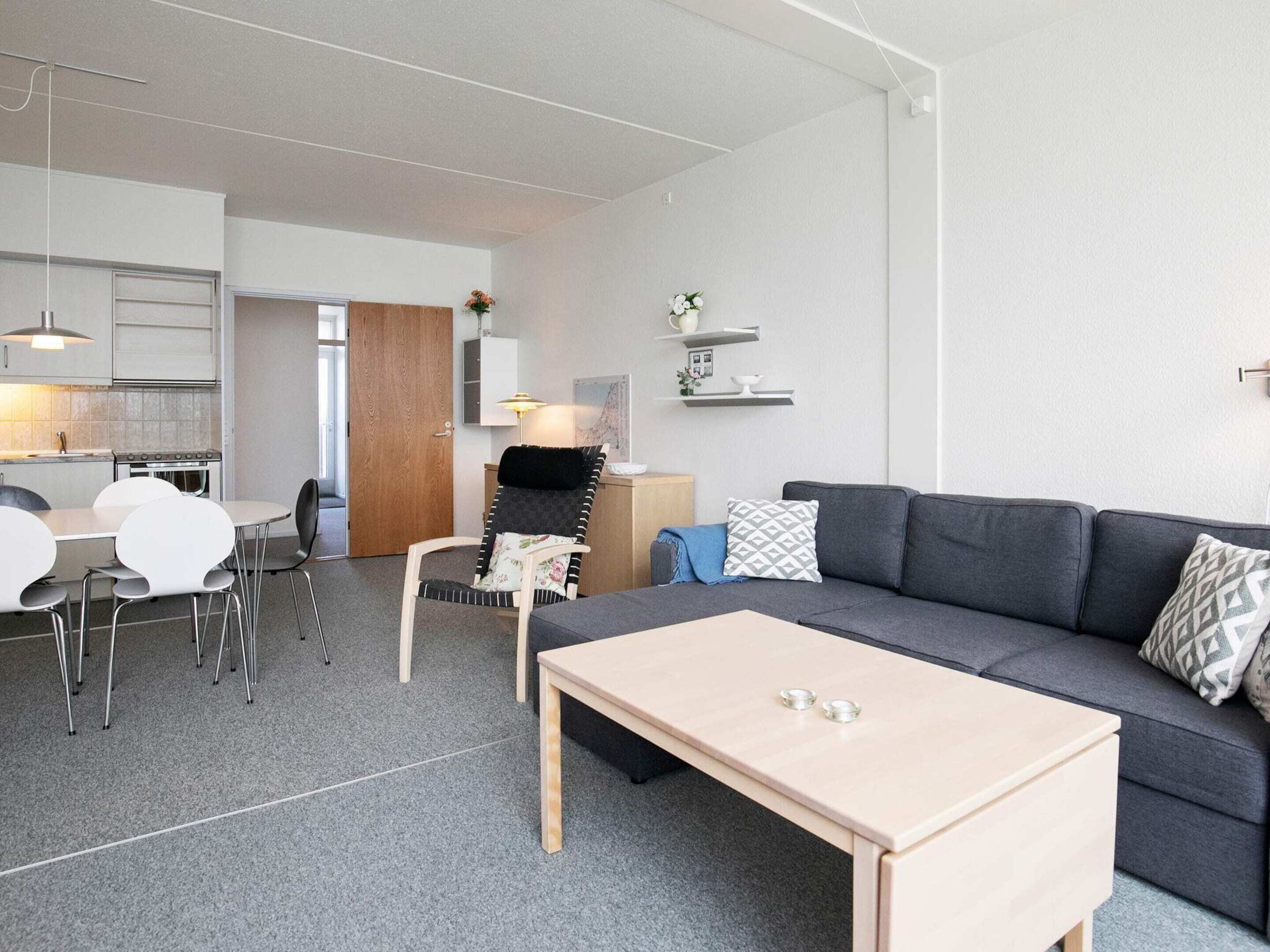Un salon moderne avec un canapé gris, une table basse en bois et un coin repas comprenant une table et des chaises blanches.