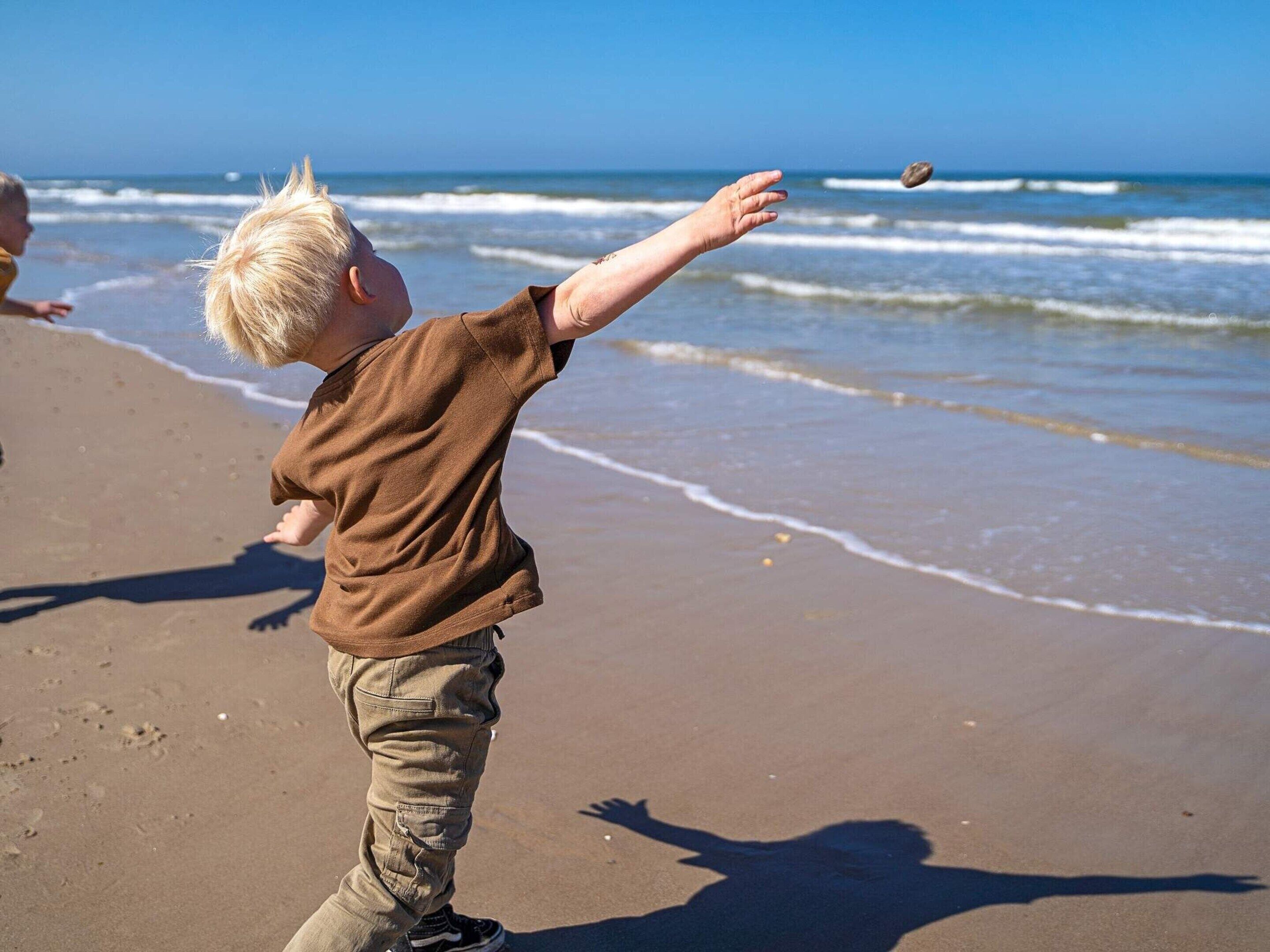 Niño jugando en una playa arenosa con olas de fondo.