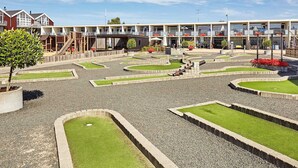 Um campo de golfe com um clube, um parquinho e um edifício com várias varandas.