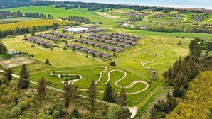 An aerial view of a residential area with multiple houses arranged in a grid pattern, surrounded by green fields and a body of water in the background.