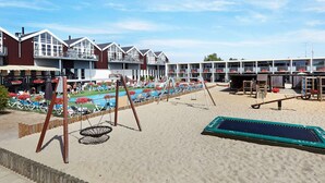 A beachside hotel with multiple balconies, a swimming pool, and beach chairs. - 5 Person Holiday Home on a Holiday Park in Glesborg (Glesborg)