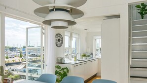 Una cucina moderna con vista su un porto turistico, una zona pranzo con sedie blu e un'ampia finestra.