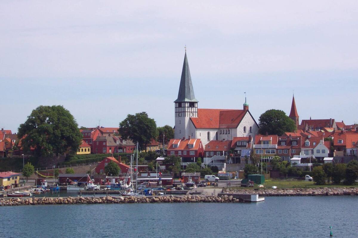 A coastal town with a prominent church steeple, red-roofed buildings, and a marina with boats.