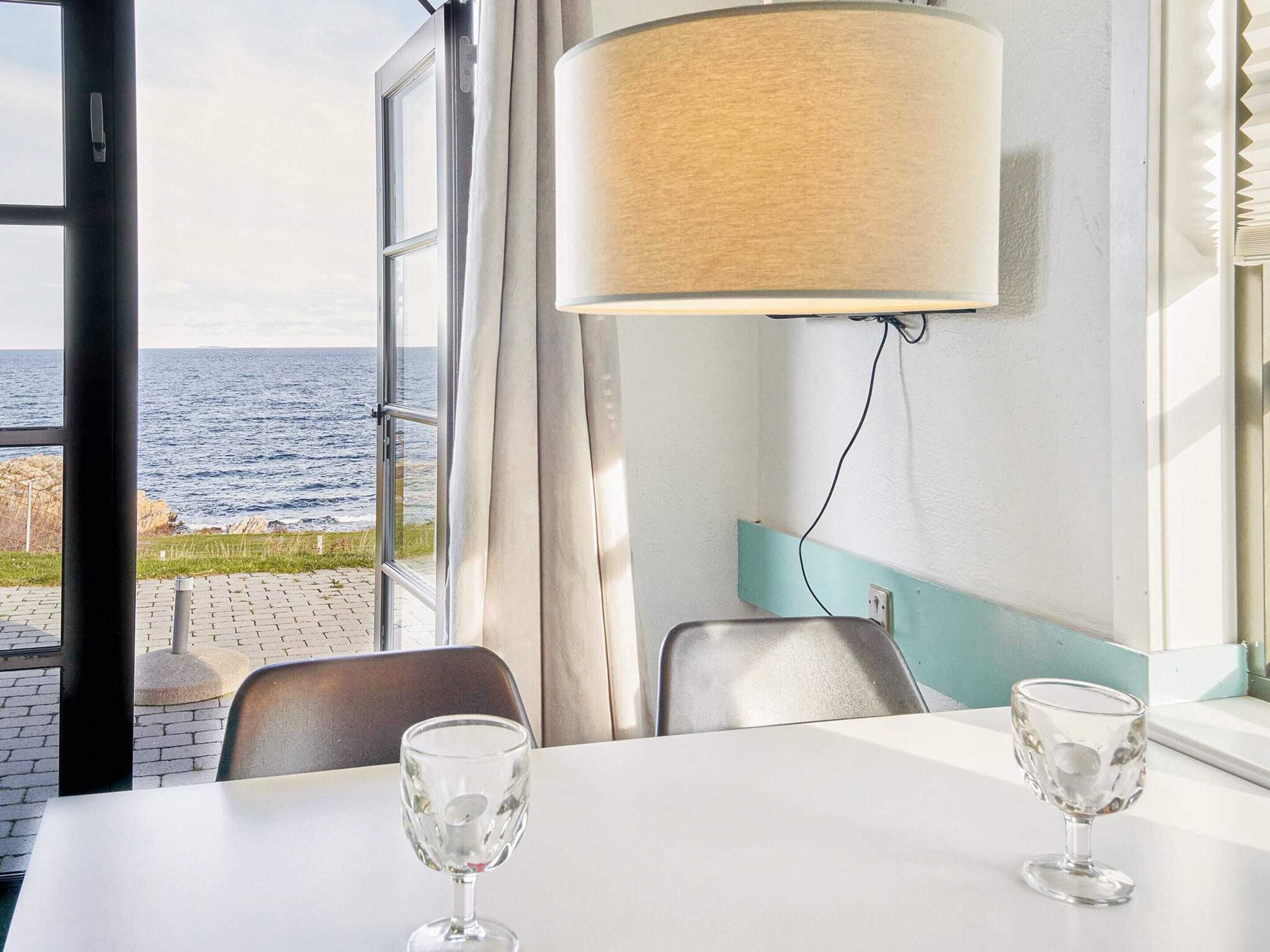 A table with two wine glasses, a lamp, and a view of the sea through a window.