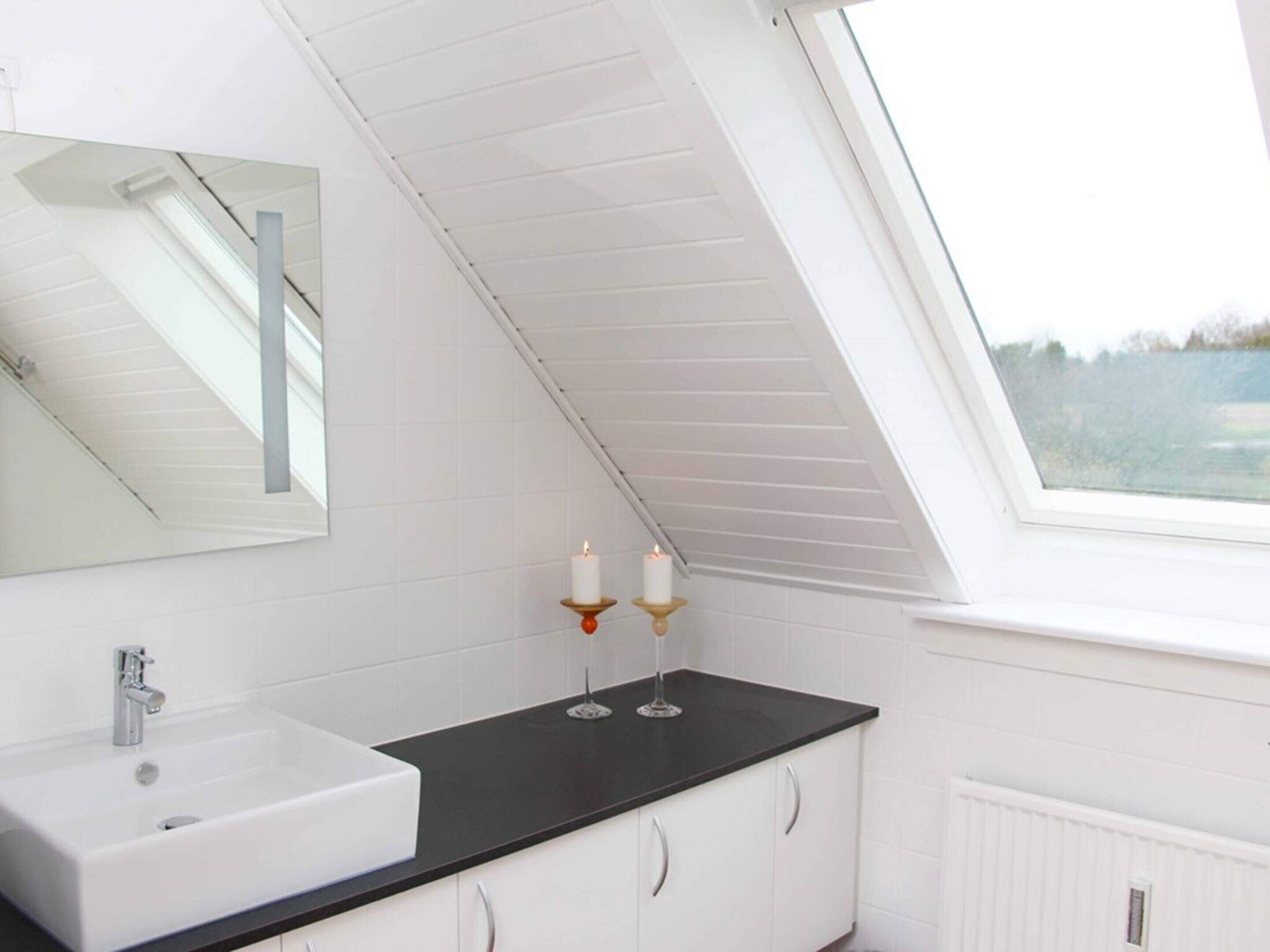 A modern bathroom with a skylight, white cabinetry, a black countertop, and a large mirror.