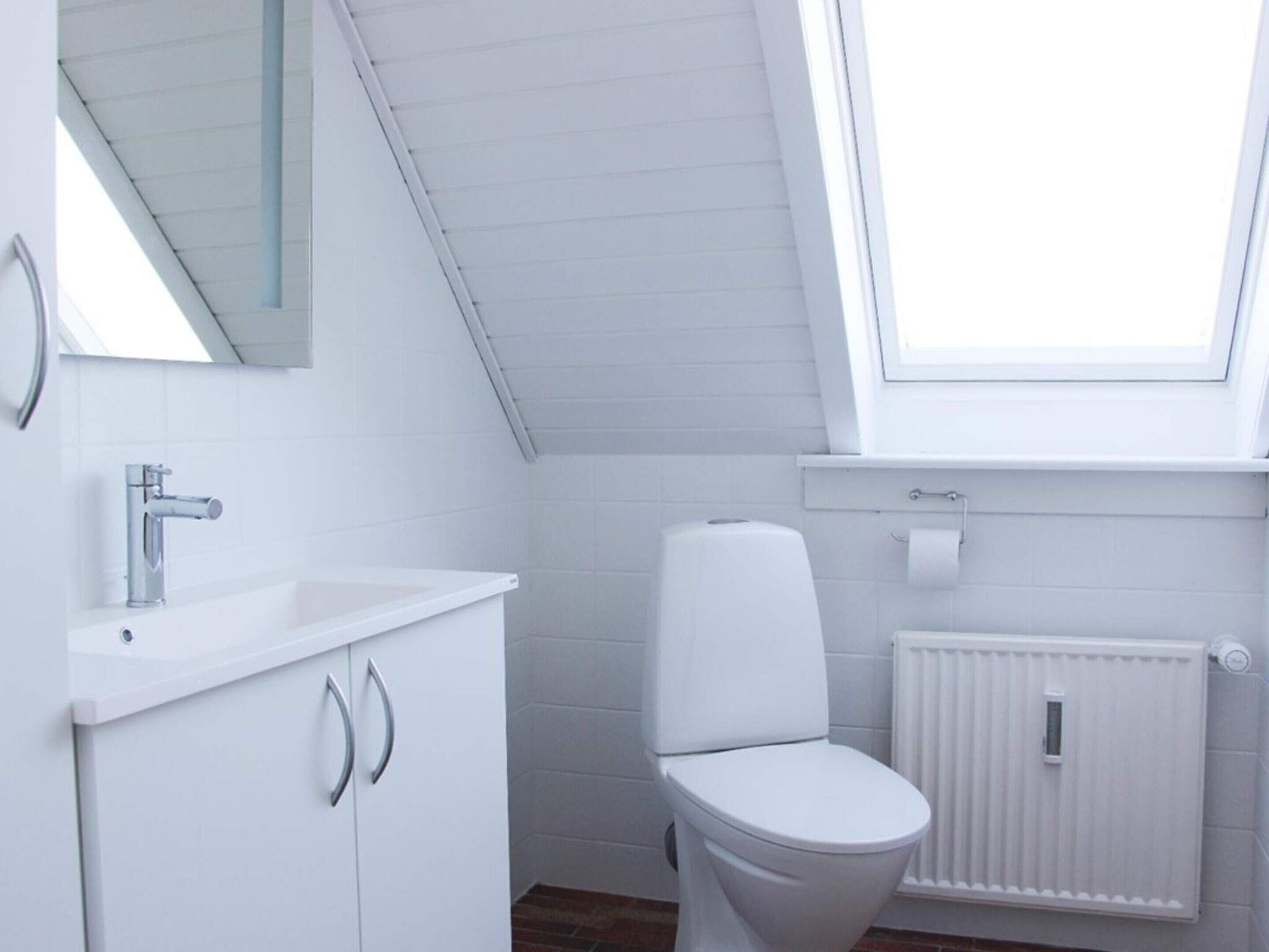 A modern bathroom with a skylight, white fixtures, and a radiator.