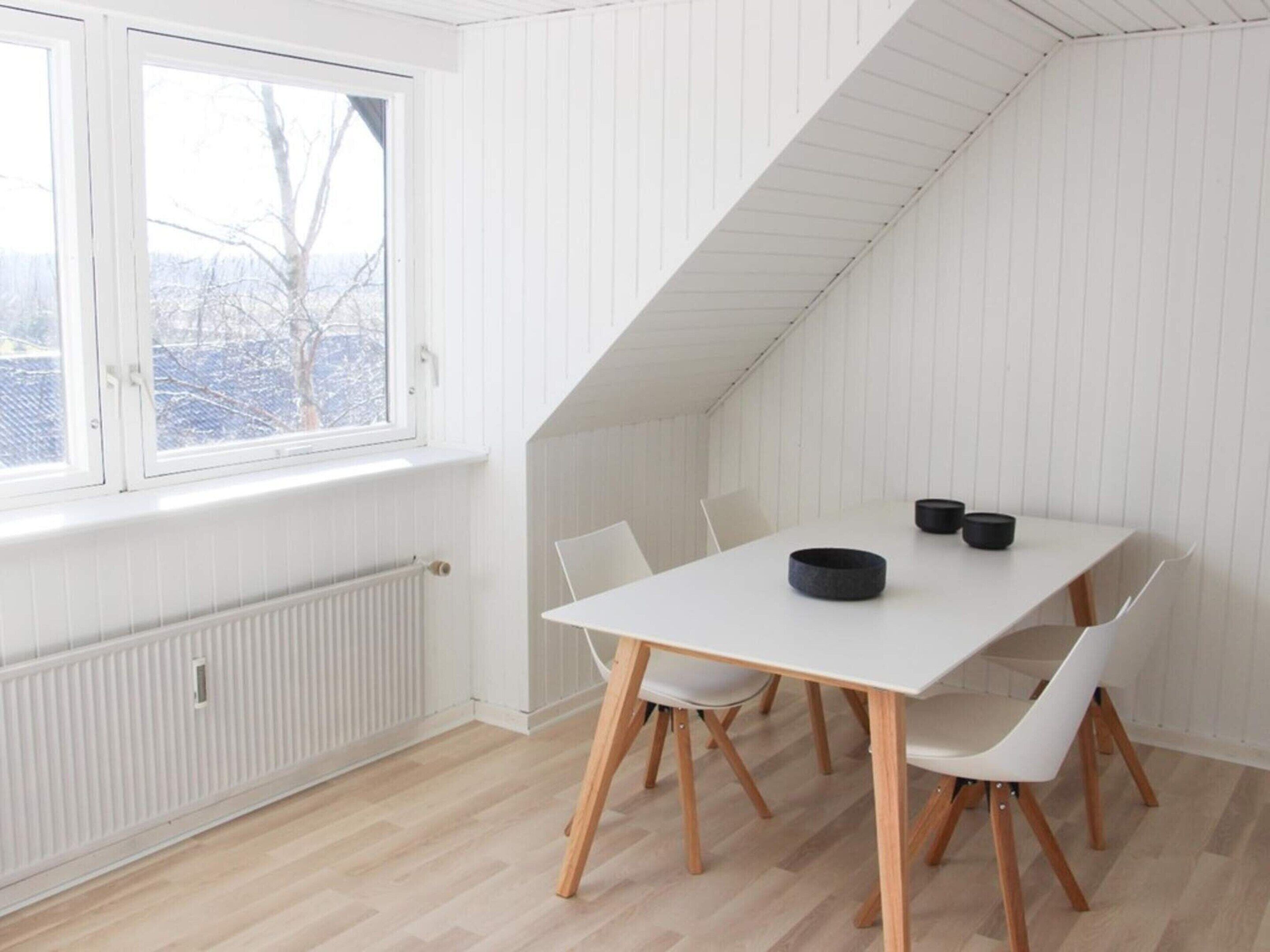A room with a white table and chairs, a window, and a sloped ceiling.
