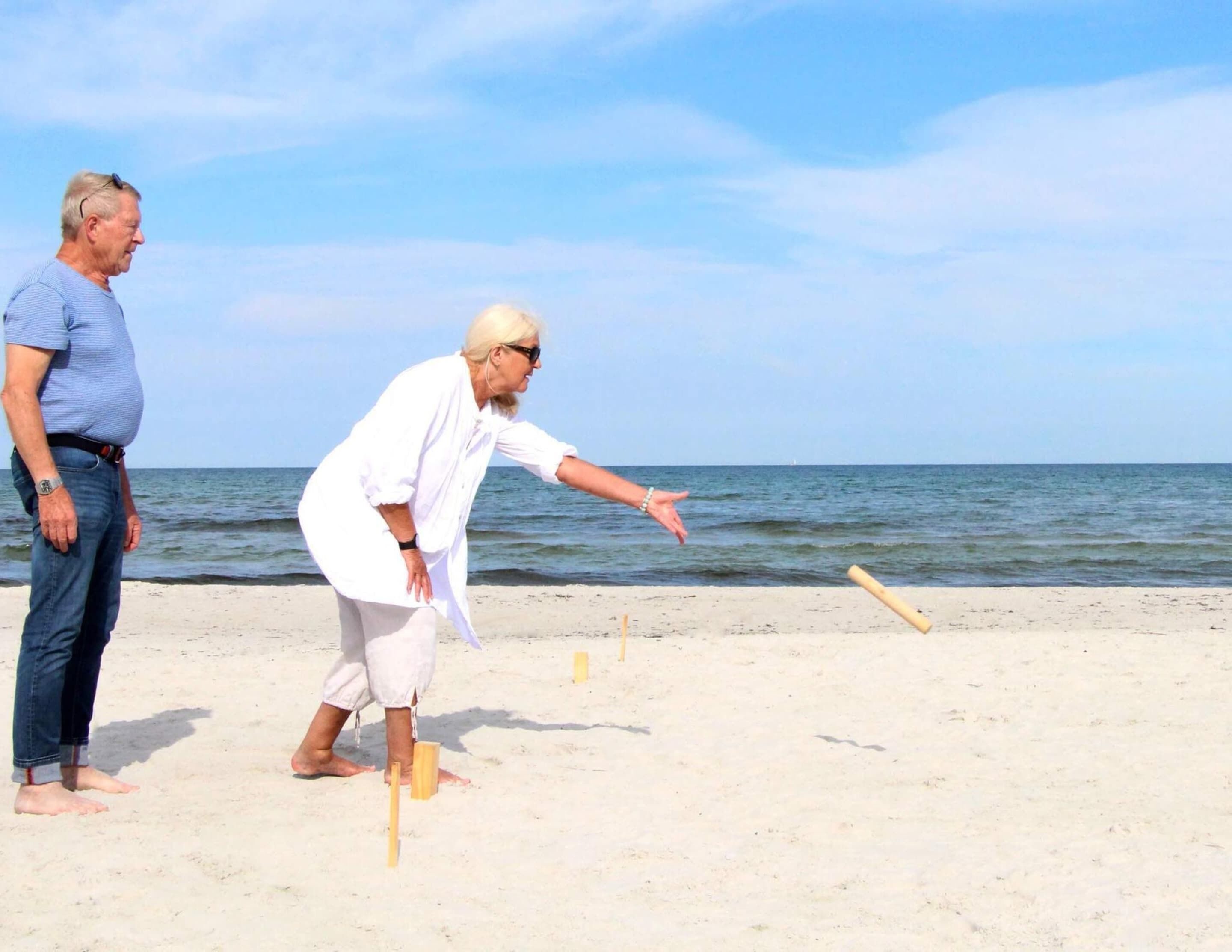 A beach with two people playing a game, one pointing at the sand.