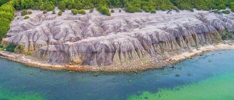 An aerial view of a coastal landscape with a rocky shoreline and a forested area in the background.