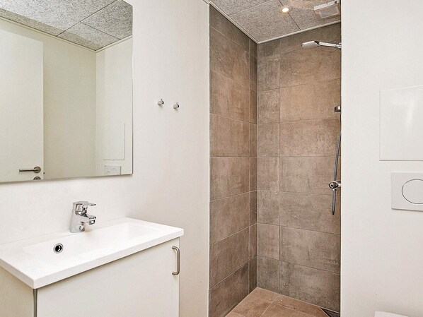 A modern bathroom with a white sink, a mirror, and a shower area with brown tiles.