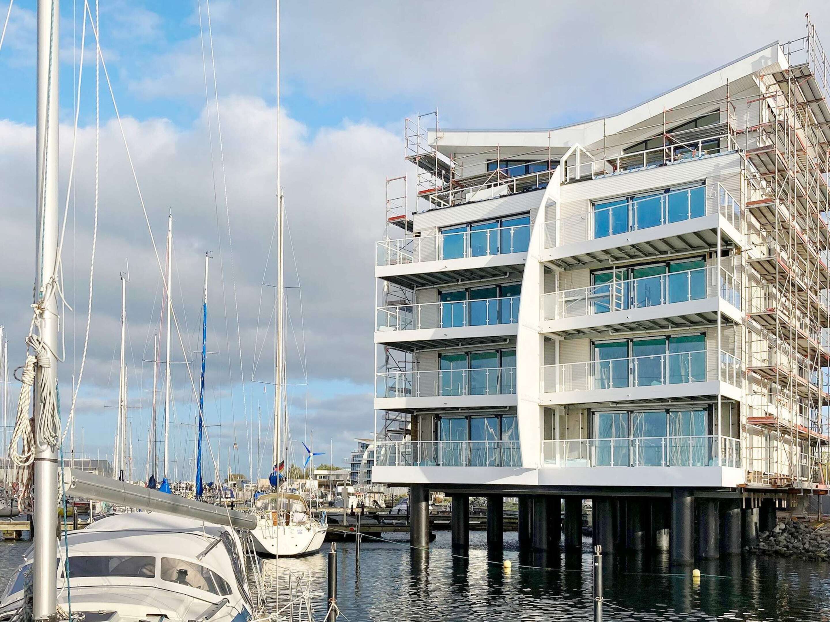 Un bâtiment situé au bord de l’eau, avec plusieurs étages, de grandes fenêtres et une zone portuaire où sont amarrés des bateaux.