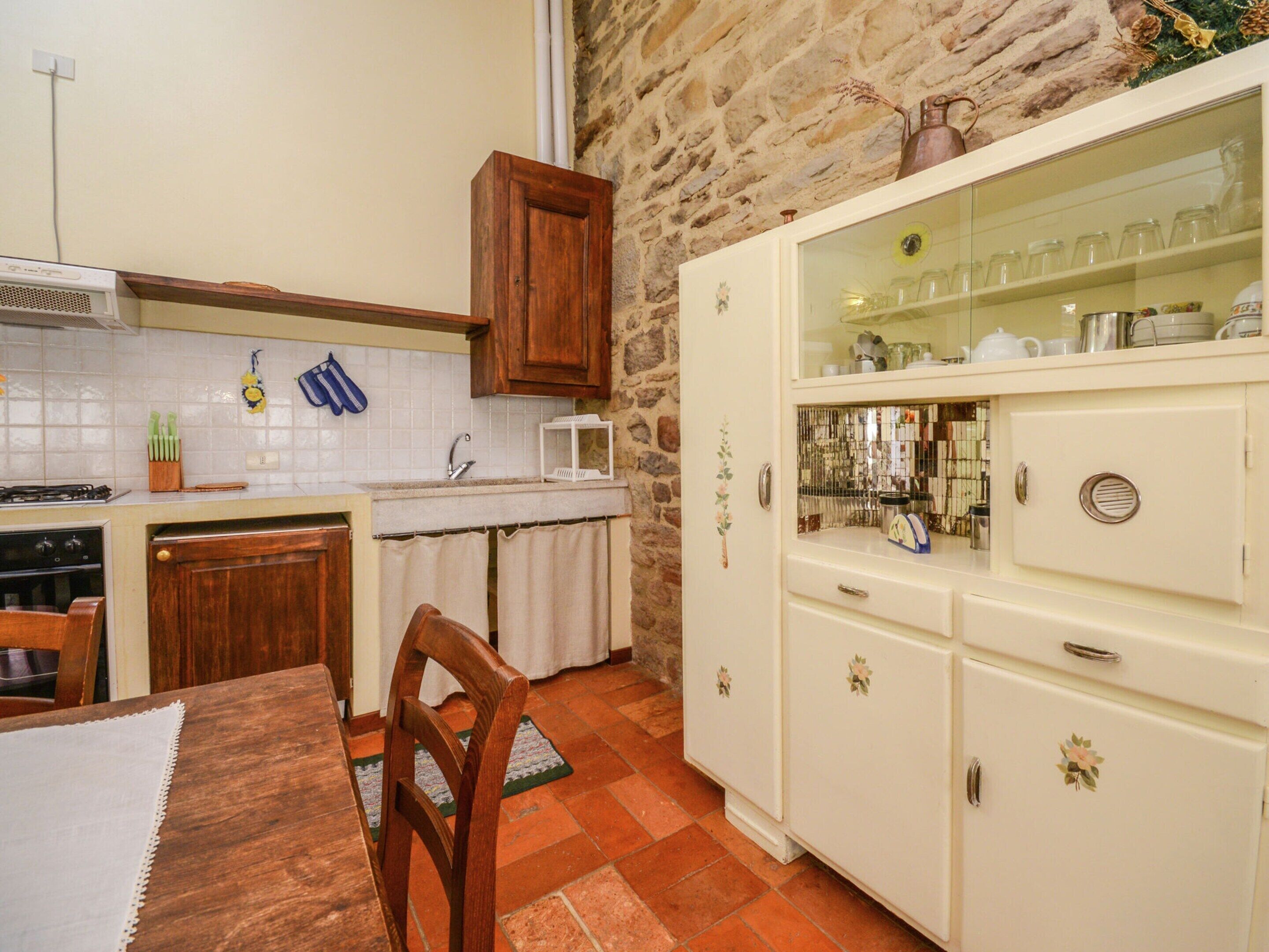 Una cocina con pared de piedra, armarios de madera, salpicadero de azulejos y una zona de comedor con mesa y sillas.