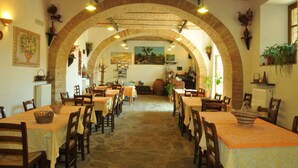 An indoor dining area with brick arches, tables with orange tablecloths, and potted plants. - Modern Holiday Home in Monte Santa Maria Tiberina (Monte Santa Maria Tiberina)